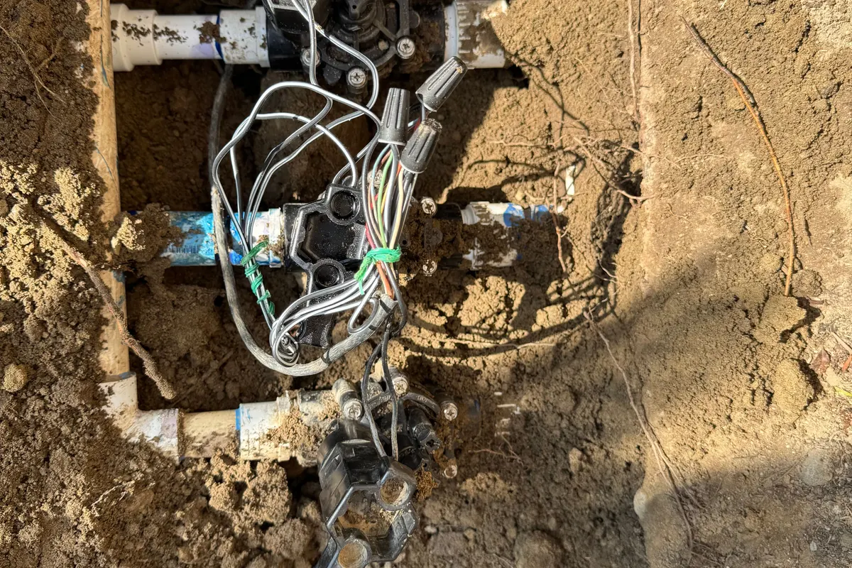 Irrigation system repair in Bakersfield, CA: valves and wiring exposed in a dug-out trench